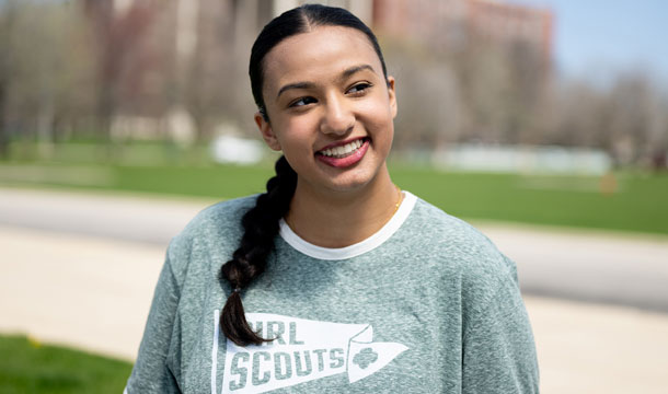 Older girl with ponytail standing outside wearing gray shirt.
