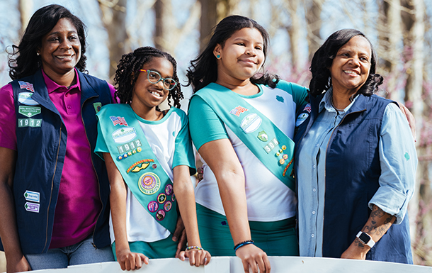 Two volunteers with two Girl Scouts standing outdoors.